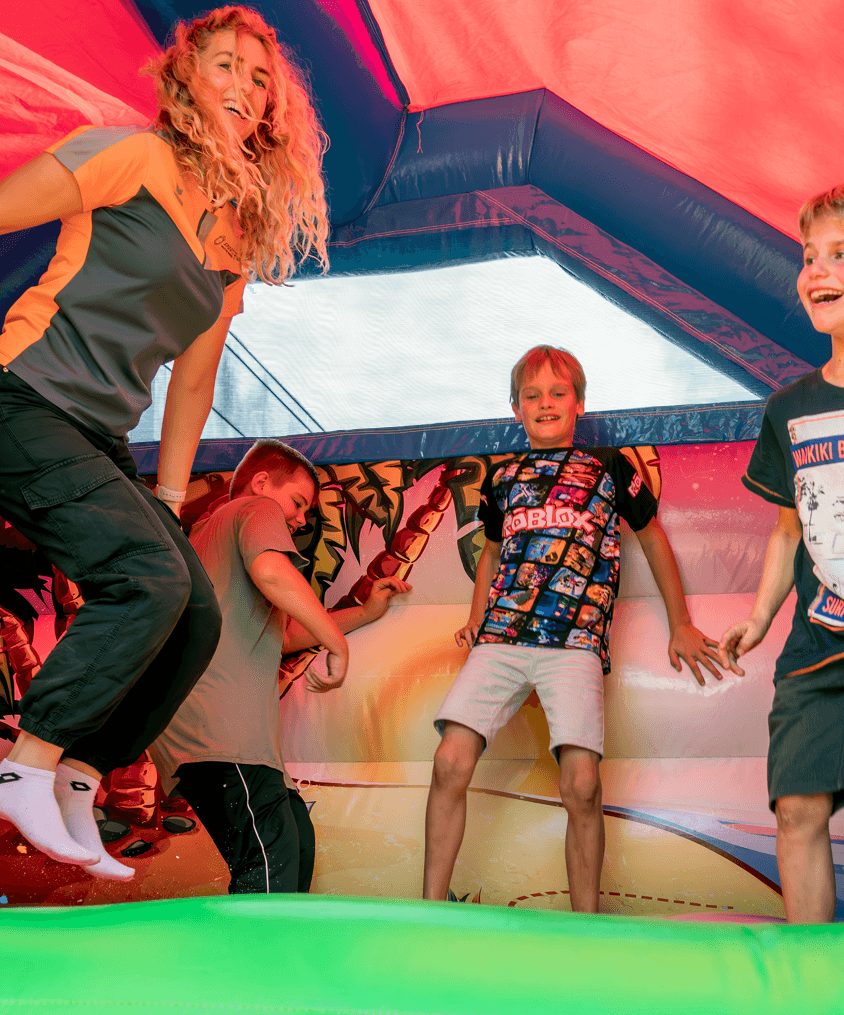 SportID buurtsportcoach springt tijdens een activiteit met kinderen op een springkussen